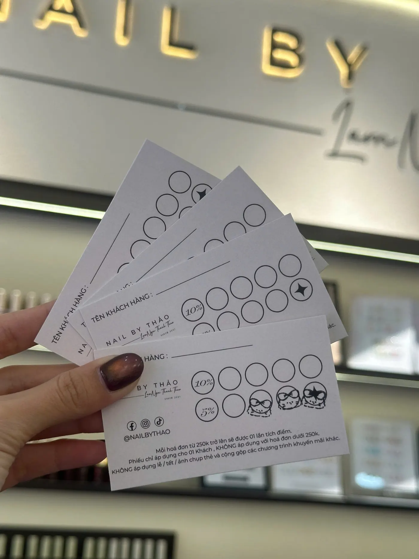 Nhân viên NAIL BY THẢO cầm phiếu tích điểm trước bảng hiệu tiệm nail Tân Bình